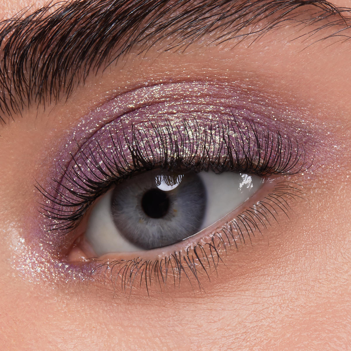Shimmering lavender eye showcases ColourPop Jelly Much Shadow Big Ego, a metallic purple with gold sparkle, swept across the lid and inner corner on long lashes; macro close-up highlighting a glossy, high-shine finish.