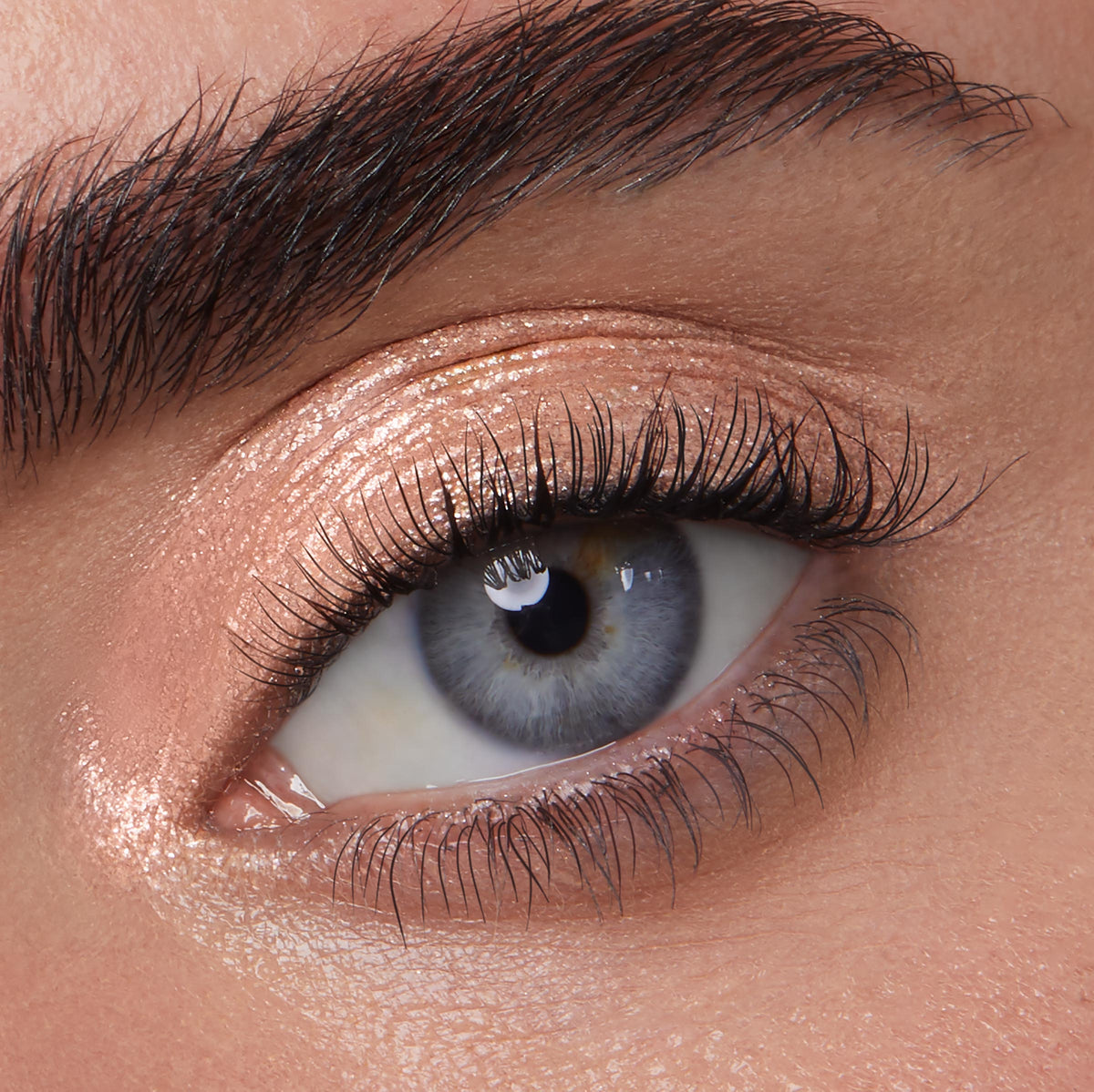 Rose-gold shimmer eyeshadow gleams on a blue-gray eye, showcasing Mystical, a ColourPop Jelly Much Shadow, with wet-look metallic sheen and fine sparkle swept across lid and inner corner in a close-up beauty shot.