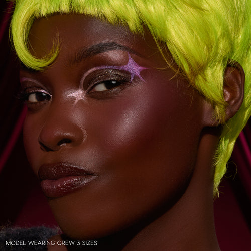 Person with bright green hair and purple makeup against a dark background