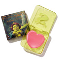 Heart-shaped pink True Love’s Form ColourPop Lip and Cheek Balm sits open in a translucent neon-yellow compact with an embossed S logo, placed beside its ColourPop x Shrek box featuring Princess Fiona artwork.