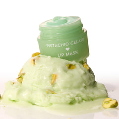 Mint-green Pistachio Gelato lip mask jar, lid off to reveal glossy balm, perched on a melting scoop of pistachio gelato with nut pieces on a white background - ColourPop Lip Mask product shot emphasizing creamy texture and dessert-inspired scent.