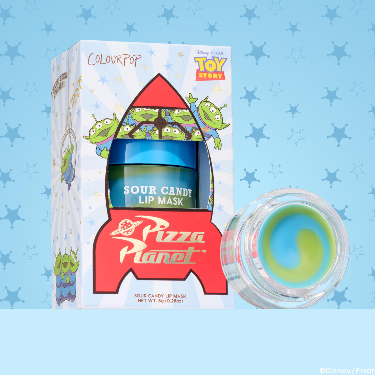 ColourPop Lip Mask The Chosen One sits in a Toy Story Pizza Planet rocket box with green alien art, showing the Sour Candy jar and an open pot revealing a blue‑green swirl balm, 8 g (0.28 oz), against a blue sheriff‑star patterned background.