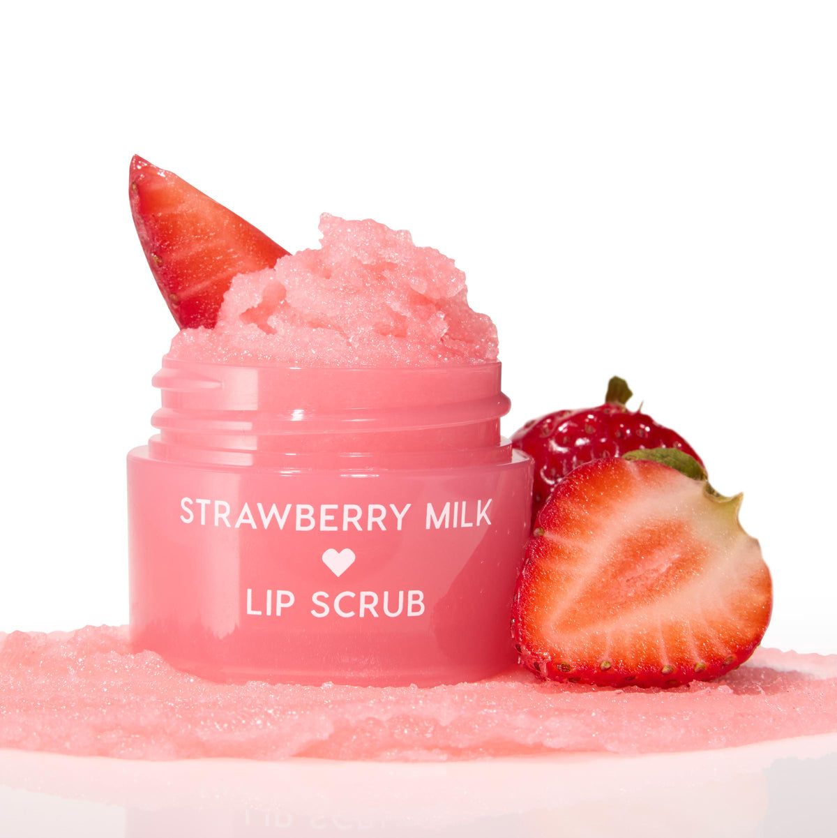 Strawberry Milk ColourPop Lip Scrub in a glossy pink jar, open with a mound of pink sugar crystals topped by a strawberry slice, resting on a swatch of scrub with fresh strawberries beside it on a white background.
