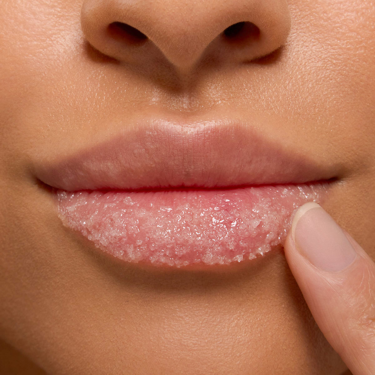 Strawberry Milk ColourPop Lip Scrub being applied as a fingertip massages pink sugar crystals across the lower lip in a tight close-up, showcasing glossy exfoliation and soft, hydrated lips.