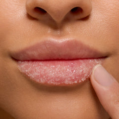 Strawberry Milk ColourPop Lip Scrub being applied as a fingertip massages pink sugar crystals across the lower lip in a tight close-up, showcasing glossy exfoliation and soft, hydrated lips.