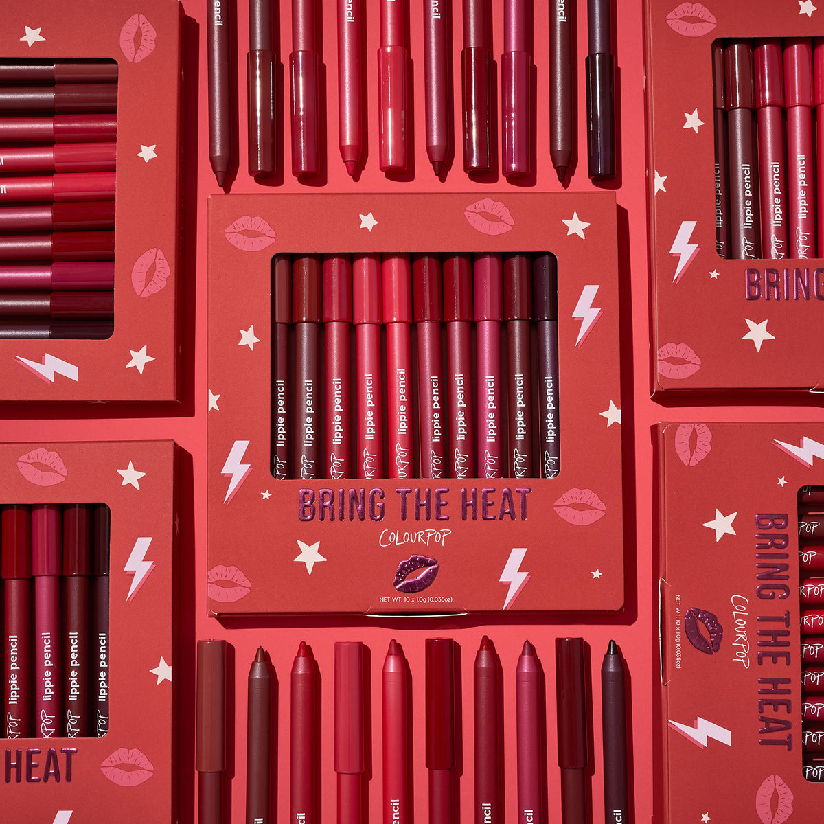 ColourPop Bring The Heat Lippie Pencil set arranged in a flat lay, showcasing creamy lip liners in reds, pinks, and berry tones; boxed and loose pencils surround the main kit on a red background with lips, stars, and lightning graphics.