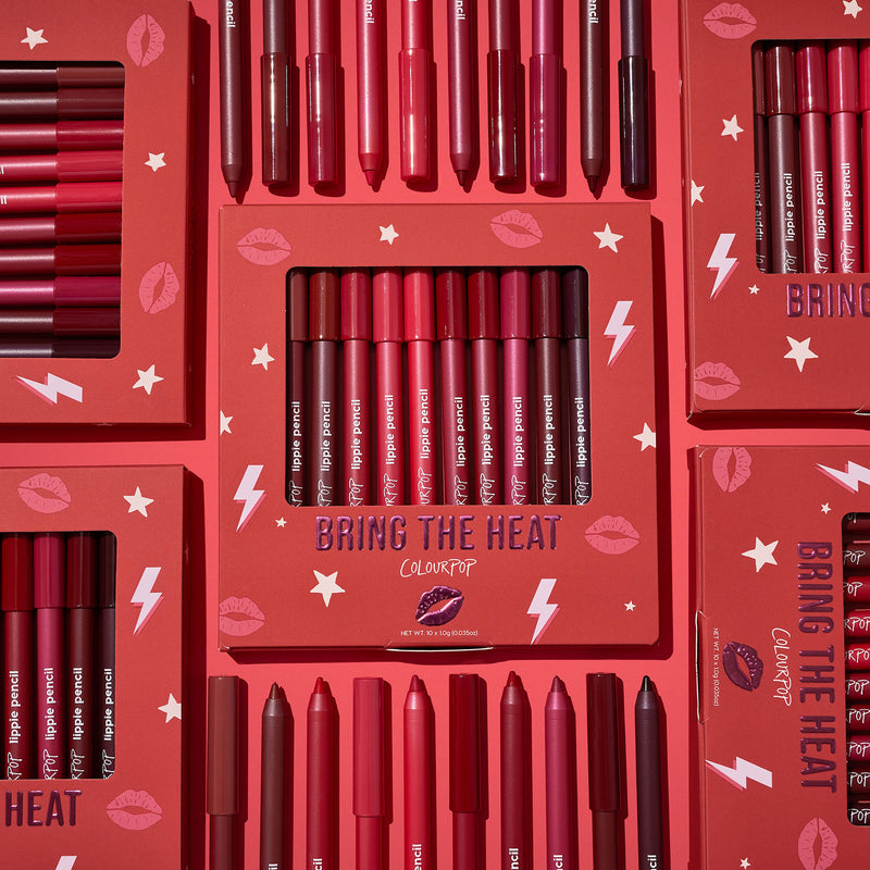 ColourPop Bring The Heat Lippie Pencil set arranged in a flat lay, showcasing creamy lip liners in reds, pinks, and berry tones; boxed and loose pencils surround the main kit on a red background with lips, stars, and lightning graphics.