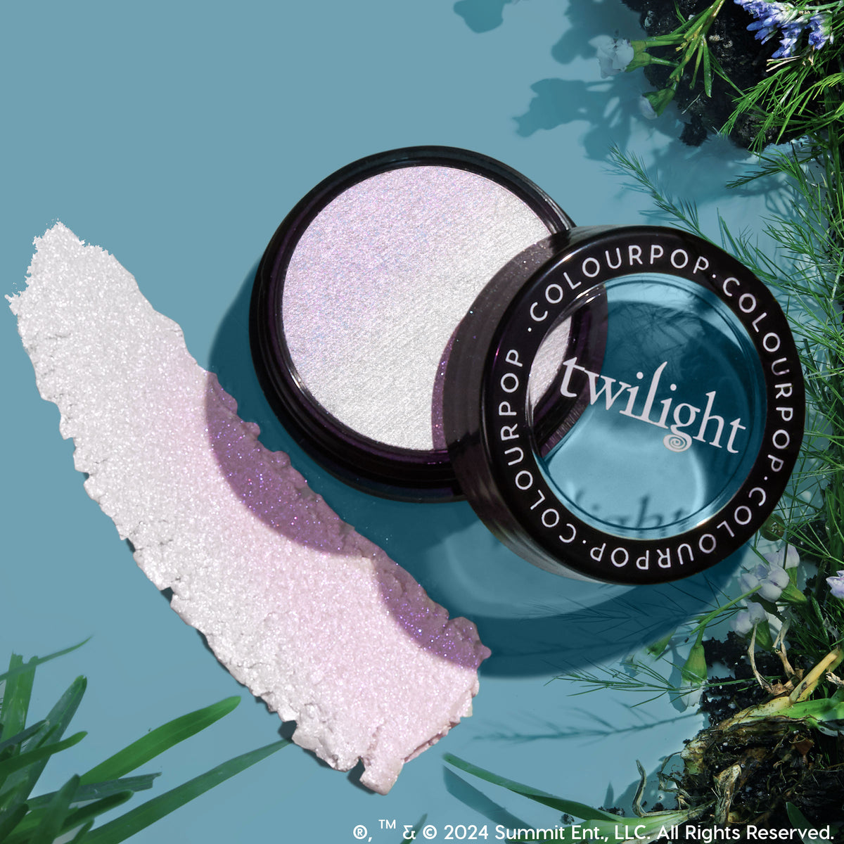 Meadow Super Shock Highlighter catches the light in an open compact, revealing an icy lavender, iridescent sheen with a pearly swatch beside it on a teal surface framed by greenery - ColourPop Super Shock Highlighter for a radiant glow.