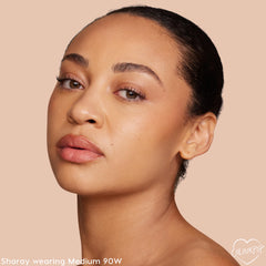 ColourPop Pretty Fresh Creamy Concealer in Medium 90W perfects a model’s complexion, showing smooth, natural coverage under the eyes and cheeks; a studio close-up on a beige backdrop highlights the warm medium shade’s skin-like finish.