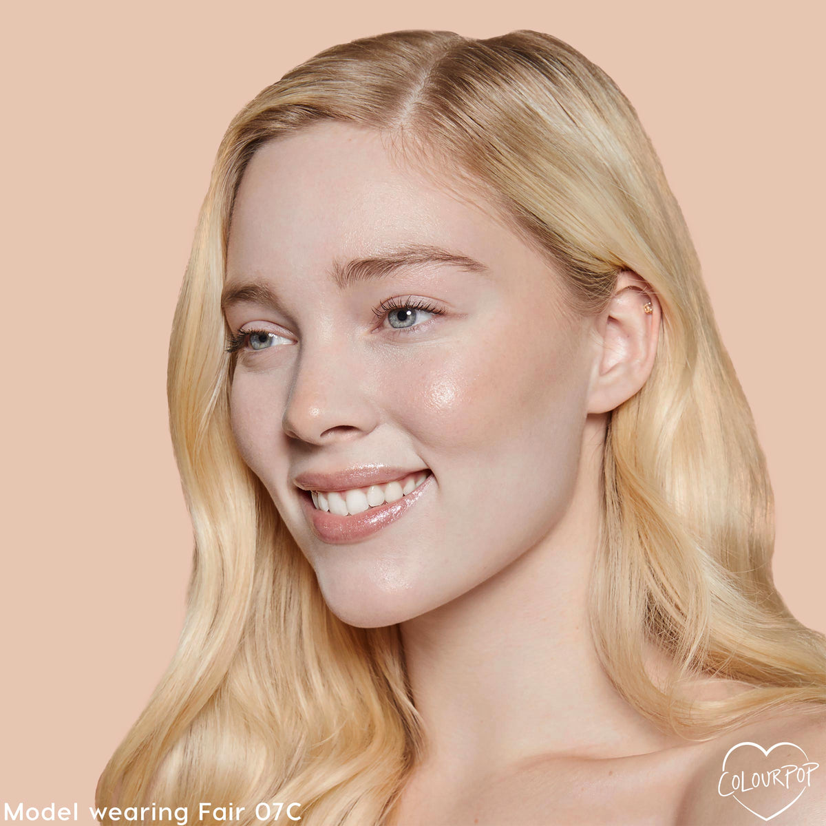 Fair 07 C shade brightening a model’s complexion with smooth, dewy medium coverage from the ColourPop Pretty Fresh Creamy Concealer, shown in a close-up against a peach backdrop to showcase even tone around eyes and cheeks.