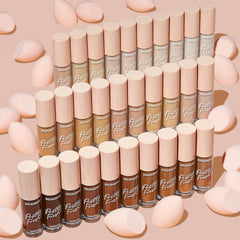 ColourPop Pretty Fresh Creamy Concealer in Fair 05 W stands in a neat grid of shades, clear tubes with blush-pink caps surrounded by soft pink makeup sponges on a nude background.
