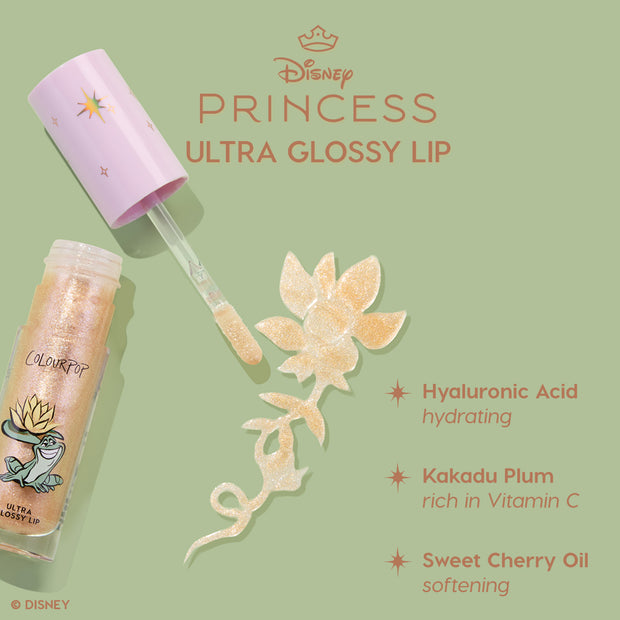 Colourpop Disney Princess Ultra Glossy Lip tube with wand swiping shimmery gold gloss in a floral swirl on a green background, highlighting hyaluronic acid hydration, Kakadu plum vitamin C, and sweet cherry oil softening benefits.