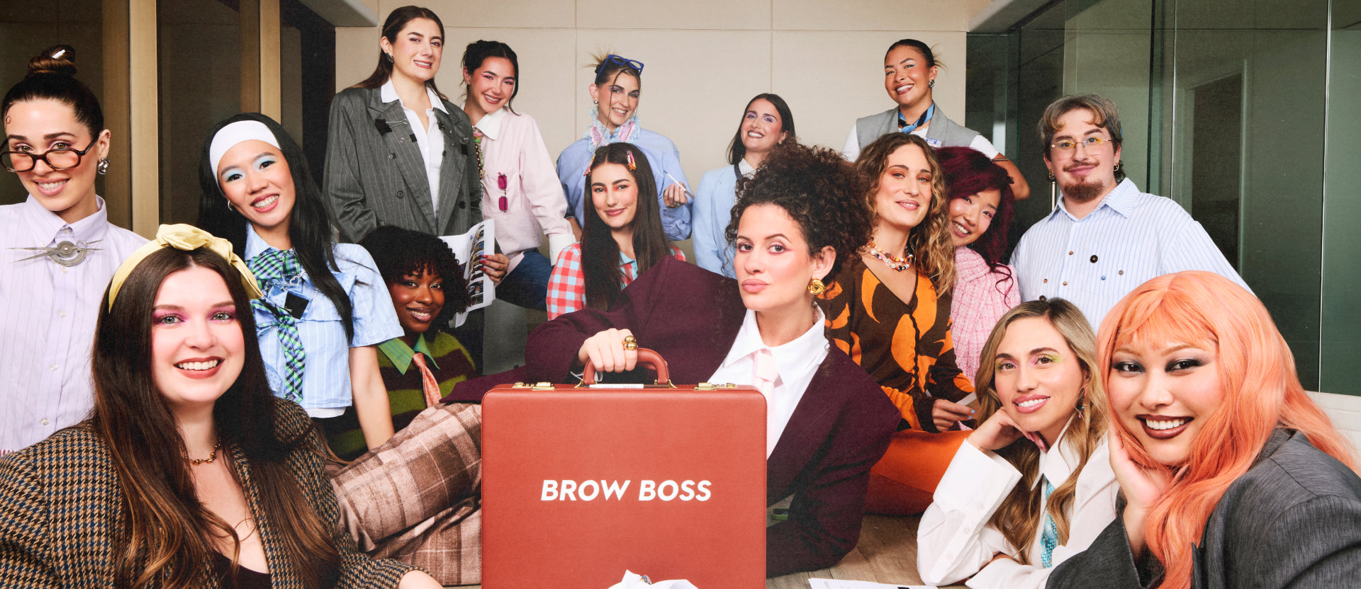 Diverse office team with bold eyebrow makeup gathers around a stylish executive holding a brown BROW BOSS briefcase, showcasing professional brow styling products in a modern conference room setting.