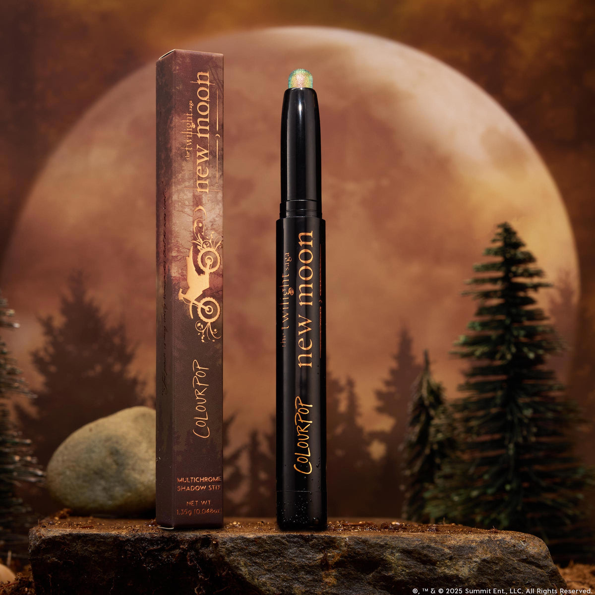 ColourPop Shadow Stix 'It’s Always Been Him' stands uncapped, revealing a shimmery green multichrome tip on a black twist-up stick with gold lettering, beside its box on a rock, framed by pine trees and a glowing full moon.