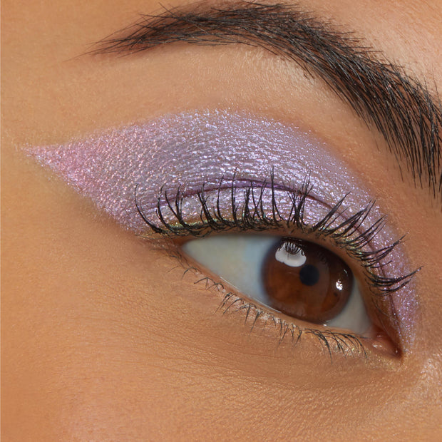 Close-up of a brown eye wearing Colourpop Cotton Candy Shadow Stix, showing shimmery pastel pink and lavender cream eyeshadow blended in a bold wing across the lid on smooth tan skin.