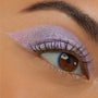 Close-up of a brown eye wearing Colourpop Cotton Candy Shadow Stix, showing shimmery pastel pink and lavender cream eyeshadow blended in a bold wing across the lid on smooth tan skin.