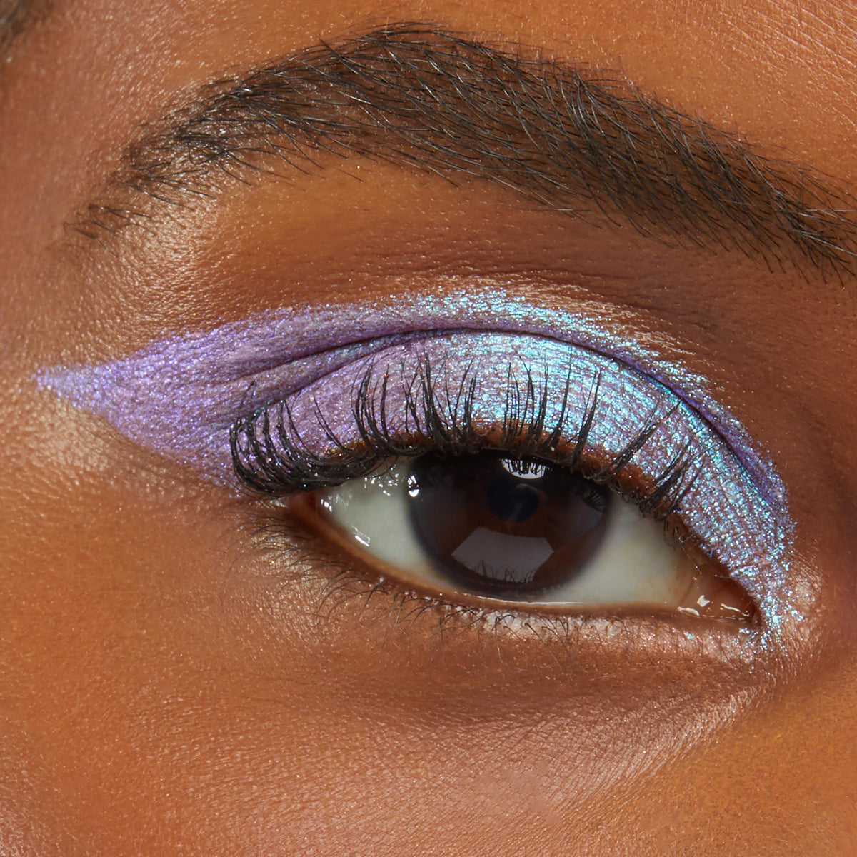 Close-up of an eye wearing Colourpop Disco Disco Shadow Stix, showcasing metallic lavender and icy blue shimmer layered across the lid and winged outwards against smooth medium-brown skin, highlighting bold, multidimensional eye makeup.