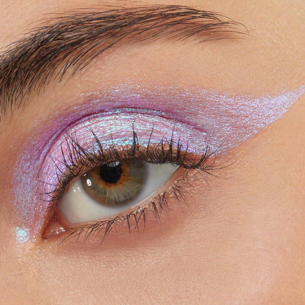 Close-up eye wearing Colourpop Disco Disco Shadow Stix, showing iridescent pink-lavender cream eyeshadow swept across the lid and extended into a sharp wing for a bold, shimmering makeup look.
