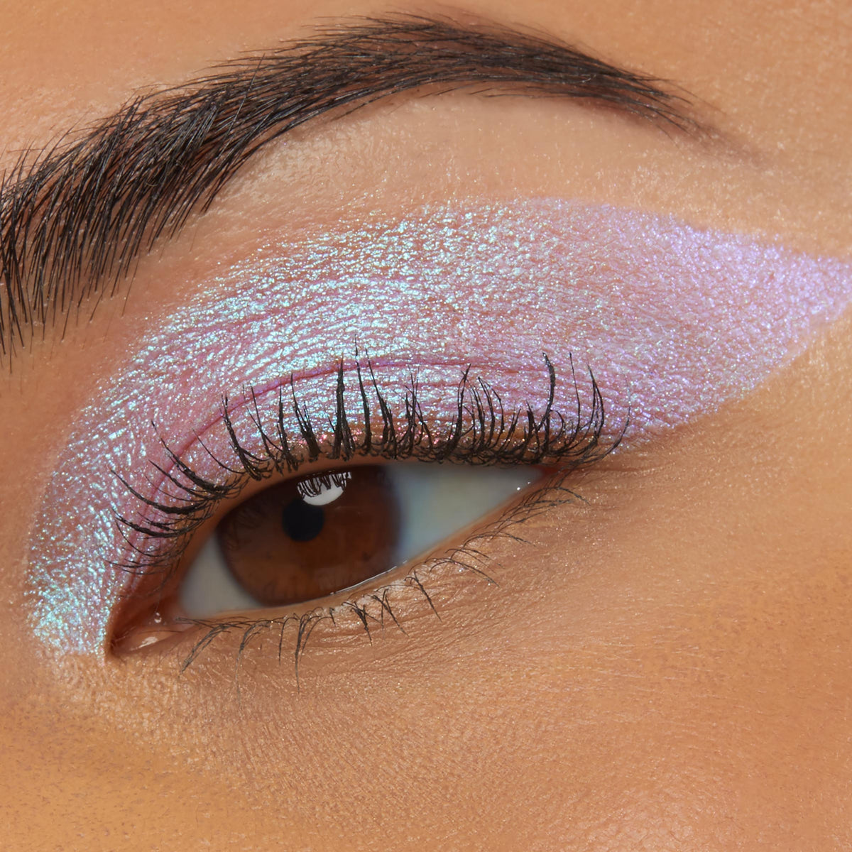 Close-up of an eye wearing Colourpop Disco Disco Shadow Stix, showing a bold wing of iridescent pink-lilac shimmer blended across the lid and crease against smooth warm-toned skin, highlighting the creamy metallic eyeshadow finish.