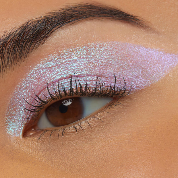 Close-up of an eye wearing Colourpop Disco Disco Shadow Stix, showing a bold wing of iridescent pink-lilac shimmer blended across the lid and crease against smooth warm-toned skin, highlighting the creamy metallic eyeshadow finish.