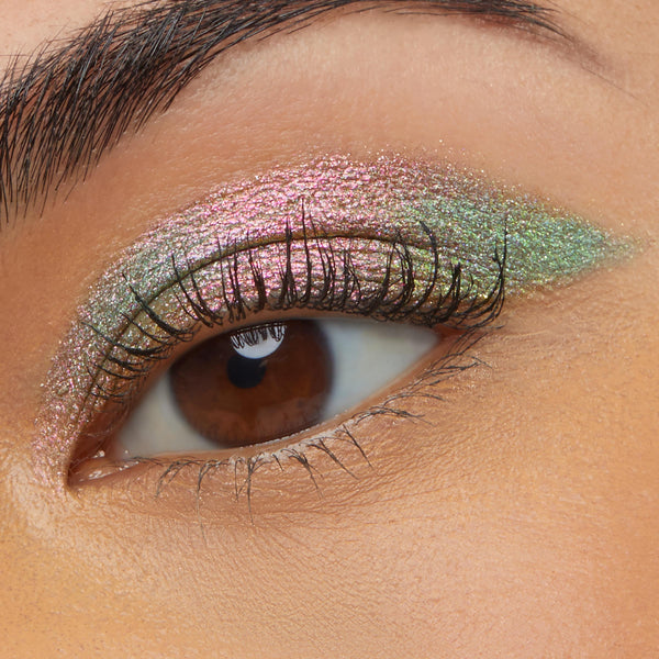 Close-up of a brown eye wearing Colourpop Galaxy Shadow Stix, showing a smooth swipe of metallic duochrome pink-to-green shimmer eyeshadow across the lid for a bold, iridescent makeup look.