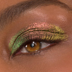 Close-up eyelid showcasing It's Always Been Him Shadow Stix, a ColourPop Shadow Stix shade, with multichrome pink, green, and gold metallic shimmer sweeping across the lid and crease on a brown eye, smoothly blended with fine sparkle.