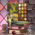 Shrek-Spress Yourself ColourPop Lip and Eye Set showcasing an open 15-pan green and neutral eyeshadow palette with Shrek artwork and a gingerbread-man lip gloss, posed on stacked storybooks by a castle window with tiara and rose.