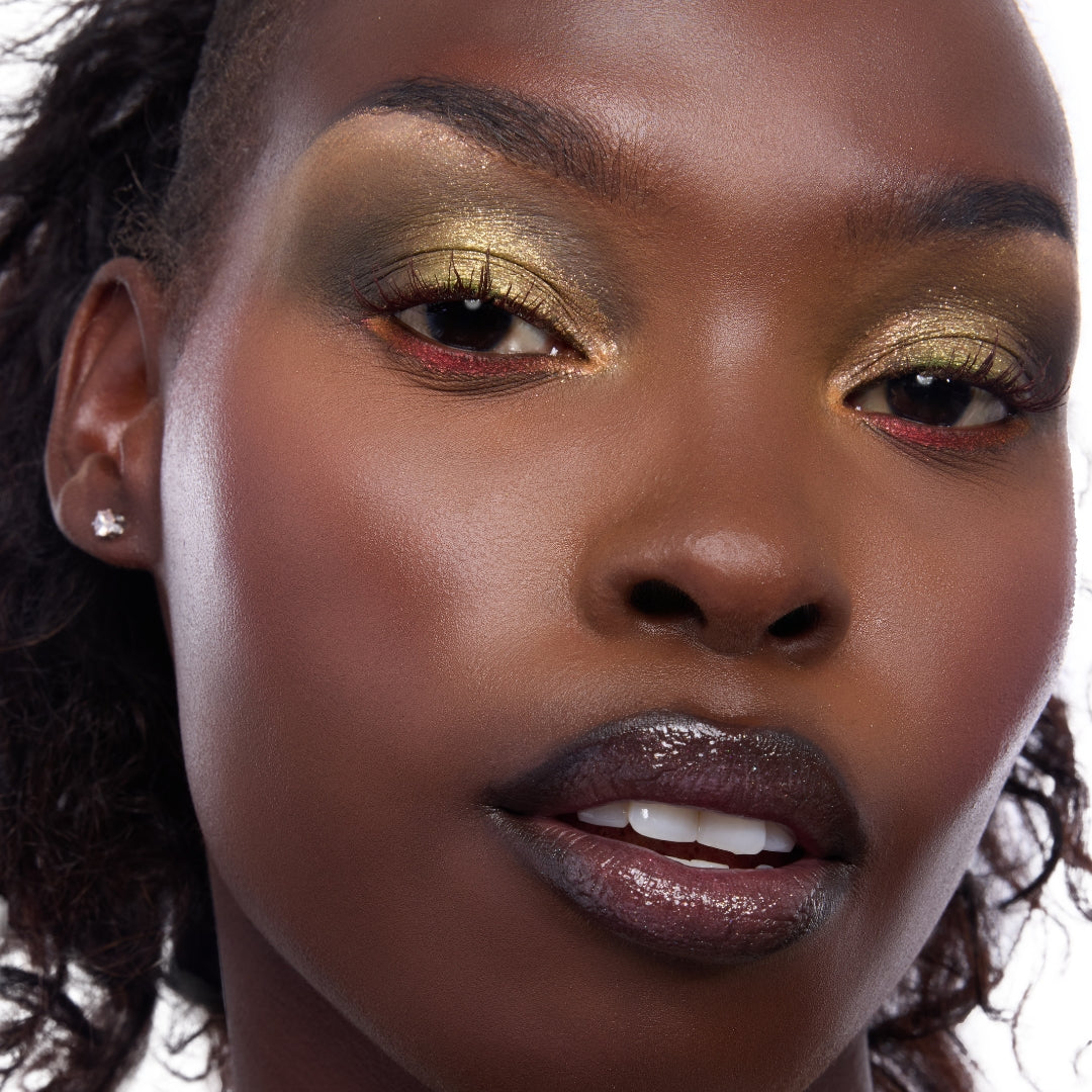 Model showcasing Shrek-Spress Yourself ColourPop Lip and Eye Set, wearing shimmering olive-gold eyeshadow with red lower-lash accents and glossy deep plum lips in a tight studio close-up.