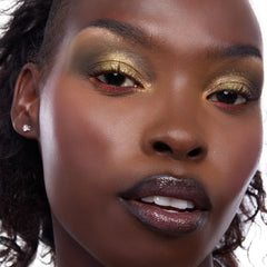 Model showcasing Shrek-Spress Yourself ColourPop Lip and Eye Set, wearing shimmering olive-gold eyeshadow with red lower-lash accents and glossy deep plum lips in a tight studio close-up.