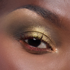 Shimmering olive-gold eyeshadow with red glitter lower liner accenting a model’s eye, showcasing the ColourPop X DreamWorks Shrek full collection set by ColourPop in a studio close-up, with smoky brown crease and sparkly inner corner.