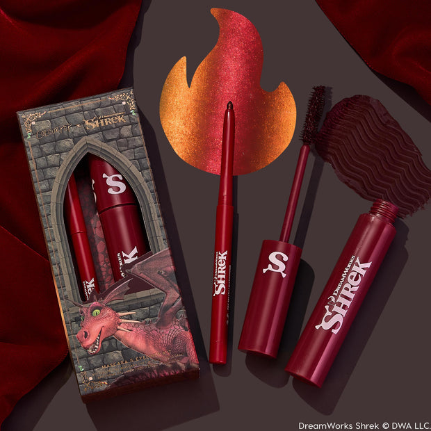 Dragon’s Keep ColourPop Crème Gel Liner extending from a red retractable pencil, with a fiery metallic crimson swatch shaped like a flame, beside matching burgundy mascara and a castle-window Shrek dragon box on a maroon backdrop.