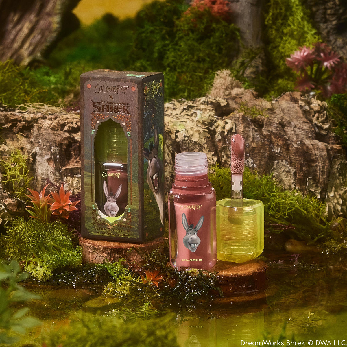 ColourPop Ultra Glossy Lip in Noble Steed, open tube with doe-foot applicator showing rosy-mauve shine, set beside Shrek x ColourPop box featuring Donkey on a mossy swamp log with water and succulents; product beauty shot for US shoppers.