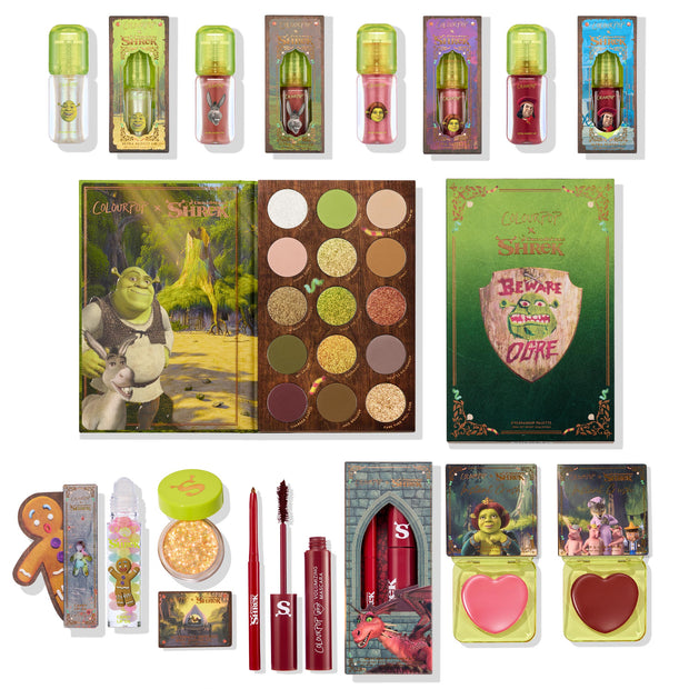 ColourPop X DreamWorks Shrek full collection set arranged in a flat lay: earthy eyeshadow palette, character lip oils and glosses, sparkle gel, red mascara and liner, and heart-shaped blush compacts with Shrek and Donkey artwork; ColourPop Full Collection Set.