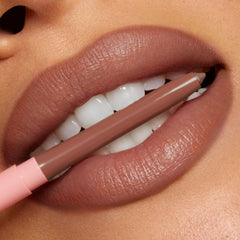 ColourPop So Juicy Plumping Lip Liner with Peptides in Tease defining full lips as the nude-brown pencil, with a blush-pink cap, is held between teeth, showcasing precise, creamy payoff and smooth contour in a studio close-up.