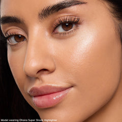Model wearing Ohana Super Shock Highlighter, showing a luminous champagne glow on the cheekbone with defined brows and glossy lips in a tight face crop; part of the Disney Lilo & Stitch Collection, ColourPop Full Collection Set.