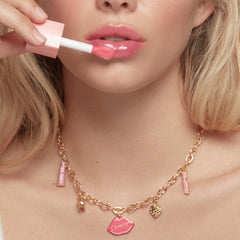 Doe-foot applicator spreads ColourPop So Juicy Plumping Glossy Lip Oil, shade Trending Now, onto glossy pink lips; close-up highlights high-shine, plumping finish with a gold charm ColourPop necklace in frame.