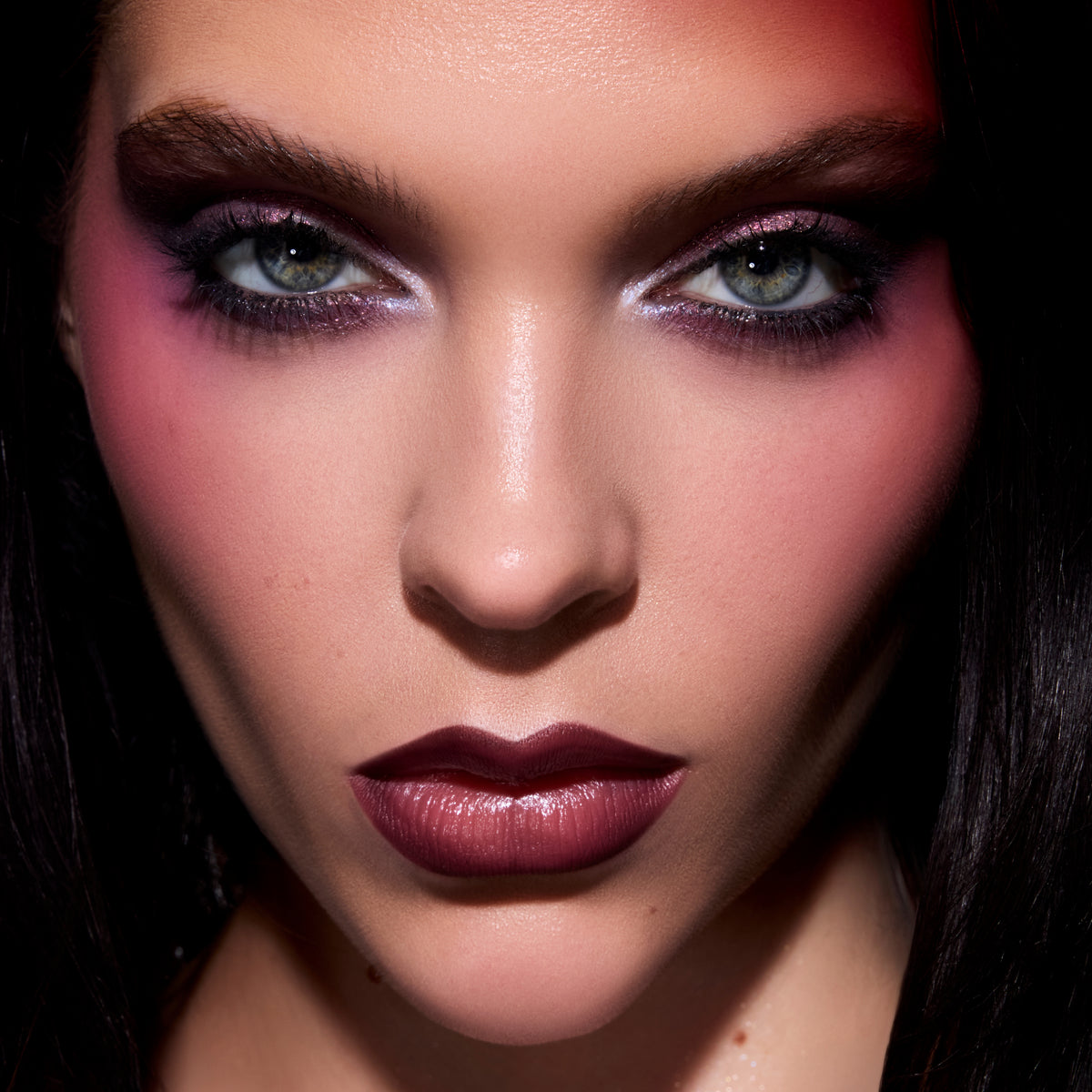 Model wearing ColourPop Just Bitten Lip Trio in a deep berry shade, lips softly glossed and paired with dramatic Twilight-inspired purple smokey eyes and flushed cheeks, shown in an intense full-face close-up beauty shot.