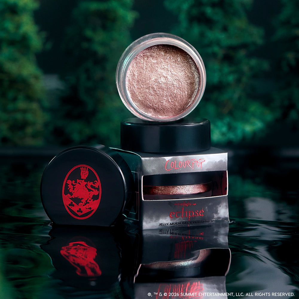 ColourPop Cullen Coven Jelly Much Shadow, a shimmery rose-bronze cream eyeshadow from the Twilight collection, opened and stacked on its Eclipse packaging against a dark, misty forest backdrop with reflections on glossy black water.