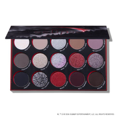 Eclipse shadow palette from the Twilight collection lying open, showing 15 circular pans of matte and glitter eyeshadows in silvers, reds, purples, and deep neutrals arranged in three rows inside a black and red themed case.