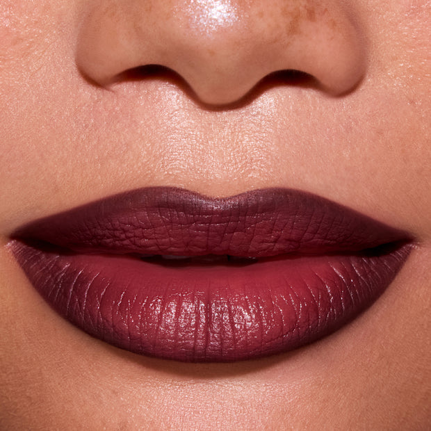 Close-up of a model’s lips wearing ColourPop New Love Lippie Stix, showing a smooth, deep berry-mauve Twilight inspired lip color with a soft satin finish against natural, freckled skin.