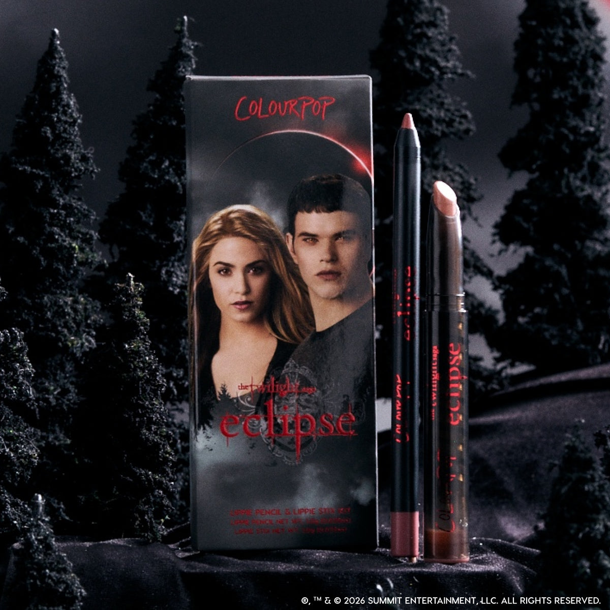ColourPop Opposites Attract Lippie Stix from the Twilight Eclipse collection standing with matching lip pencil beside character-printed box, styled in a dark, misty forest setting for a dramatic, vampy makeup look.
