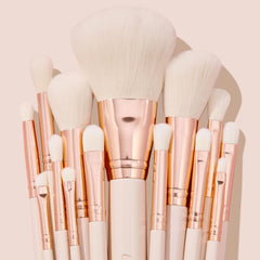Ultimate Brush Roll, a ColourPop Makeup Brush Kit, fanned upright with soft white bristles, rose-gold ferrules, and cream handles, showcasing face and eye brushes for powder, blush, and eyeshadow blending on a blush-pink studio backdrop.