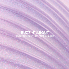 ColourPop Ultra Glossy Lip Buzzin' About swatched - sheer lavender gloss with rainbow pearl shimmer - spread in sweeping ridges across a close-up backdrop to showcase its glossy, sparkly finish.
