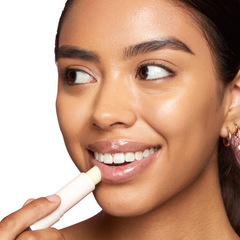 ColourPop Coconut Lip Balm glides onto lips as a model applies the creamy balm from a soft pink twist-up tube, close-up on a smiling face with a glossy finish against a clean white background.
