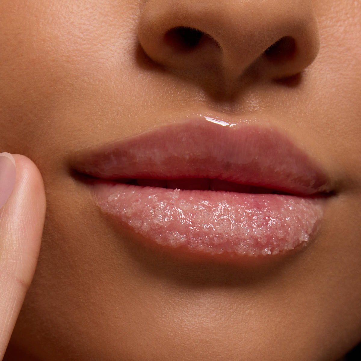 Glossy lips buffed with Neapolitan Sundae ColourPop Lip Scrub, sugar crystals exfoliating the lower lip as a fingertip applies the treatment in a close-up, revealing a smooth, hydrated finish.
