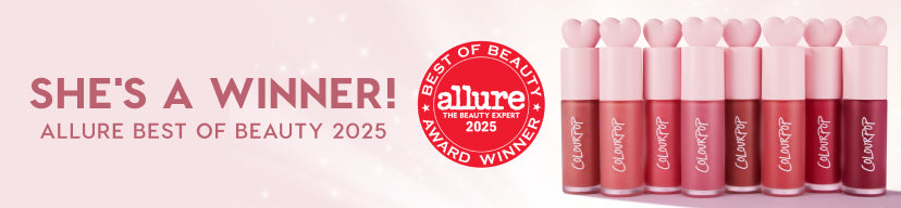 ColourPop lip products lined up in gradient nude-to-rose shades with pink heart-shaped caps, positioned beside an Allure Best of Beauty 2025 award seal and “She’s a Winner!” headline on a blush background, highlighting award-winning makeup.