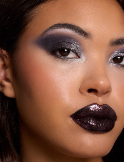 Close-up model showcasing smoky charcoal and silver eyeshadow with bold glossy black lipstick under studio lighting, highlighting high-shine texture and dramatic blend for a ColourPop glam makeup look.