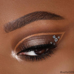 Shimmery champagne-bronze cut-crease eye makeup created with the ColourPop Feelin' Bubbly shadow palette, winged shape with black liner, long lashes, and three crystal studs at the outer corner in a tight close-up on the eyelid.