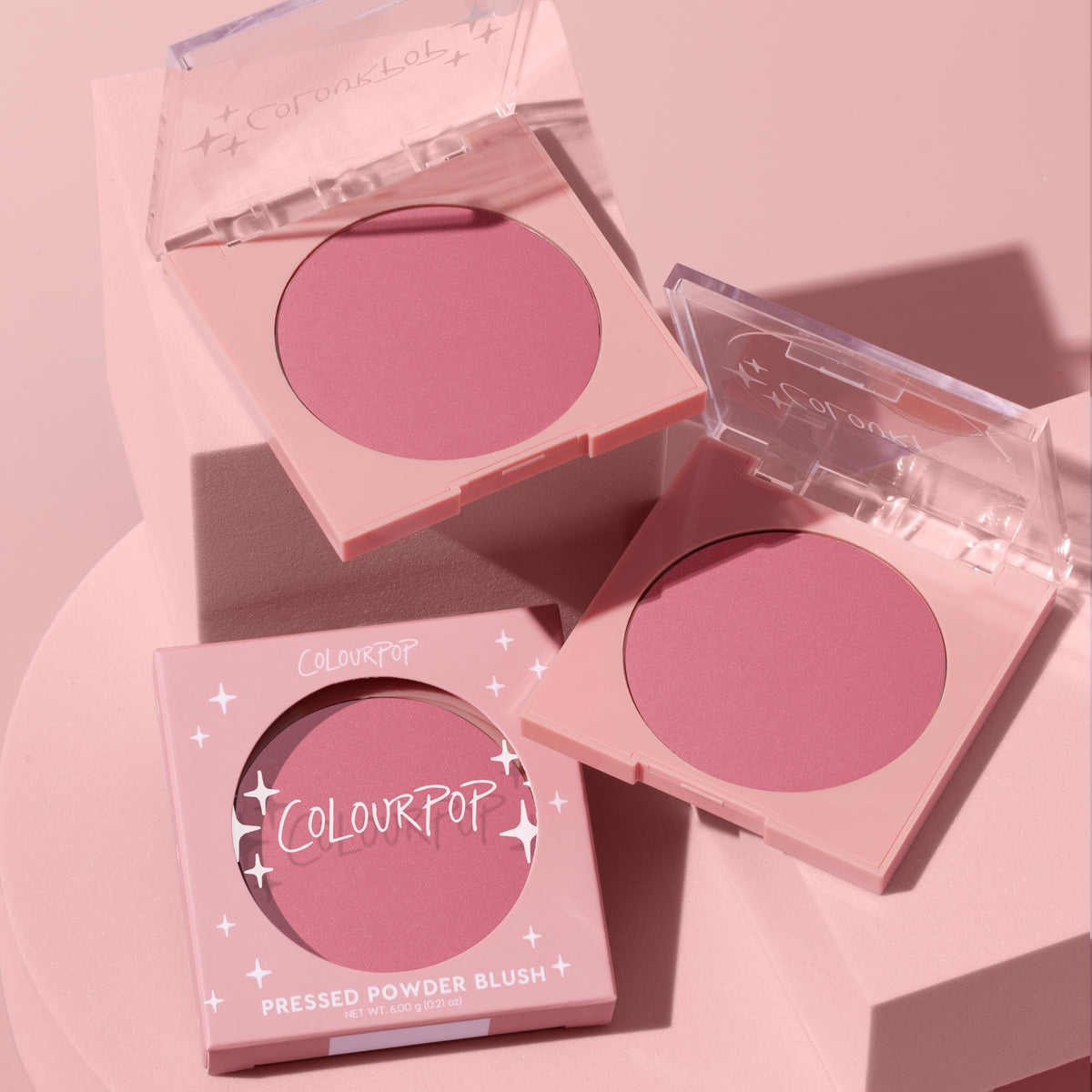 ColourPop New to U pressed powder blush compact opens to reveal a soft rosy‑mauve pan, flanked by a second open compact and a boxed unit, styled on pastel pink blocks; clear lids and star accents brand the ColourPop Pressed Powder Blush.