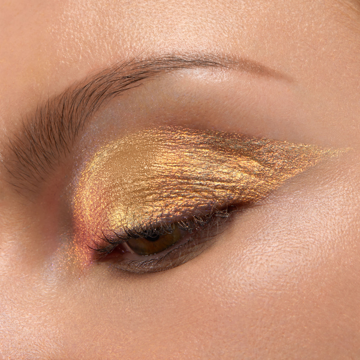 ColourPop Chrome Liquid Shadow in Sweetzer Ave swept across a closed eyelid, flashing molten gold with rose-copper shifts in a sharp wing, showcasing high-shine metallic finish and smooth, opaque payoff in a studio close-up.